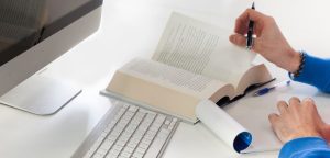 Open book on the table and person turning the page and writing something